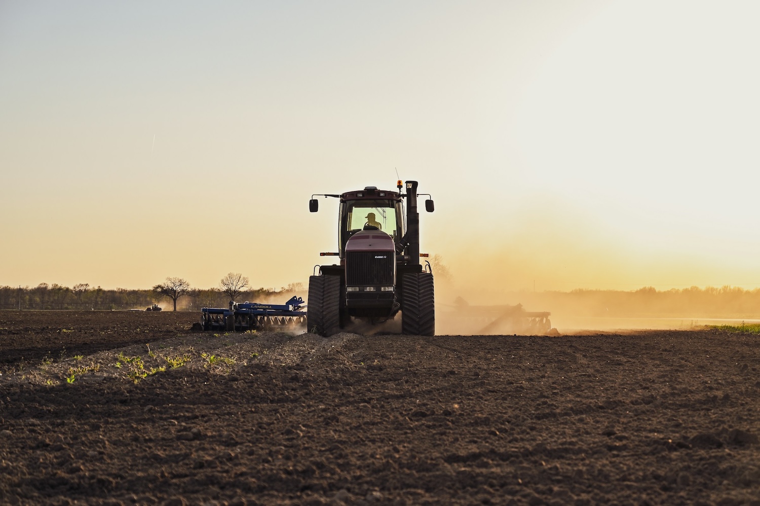 A farmer plowing his field with his tractor on a sunny day at sunset